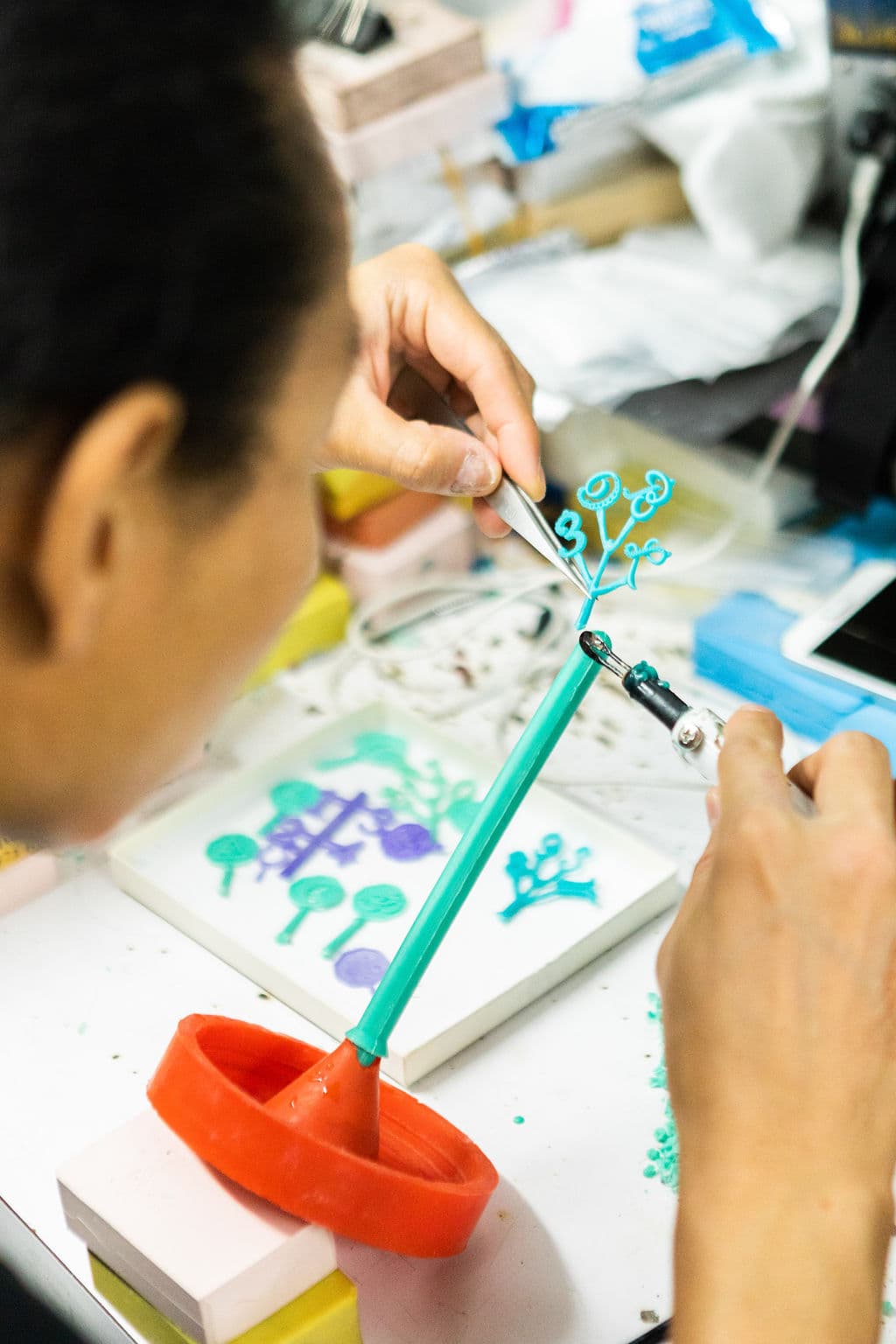 Jeweler working with a green wax jewelry pattern tree using tweezers and a handheld tool.